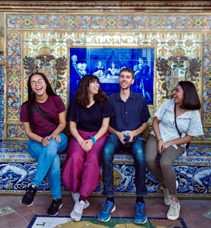 UIC students sit on a step in front of a colorful mural in Salamanca.